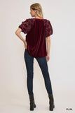 Woman wearing a burgundy velvet top with lace sleeves and dark jeans on a white background