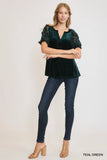 Woman wearing a teal green blouse with lace sleeves and dark jeans on a white background