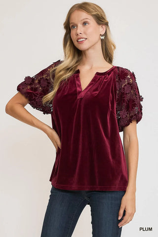 Woman wearing a burgundy velvet top with lace sleeves on a white background