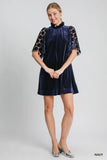 Woman wearing a navy velvet dress with lace sleeves on a gray background