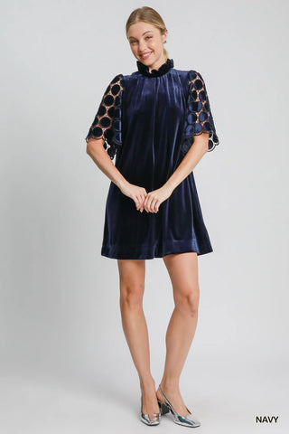 Woman wearing a navy velvet dress with lace sleeves on a gray background