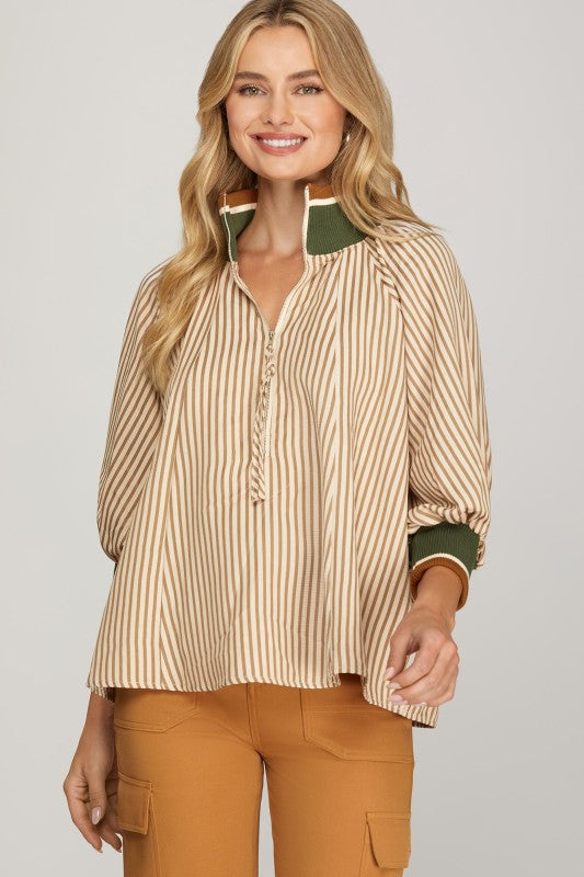 Woman wearing a striped shirt with green accents and brown pants on a plain background