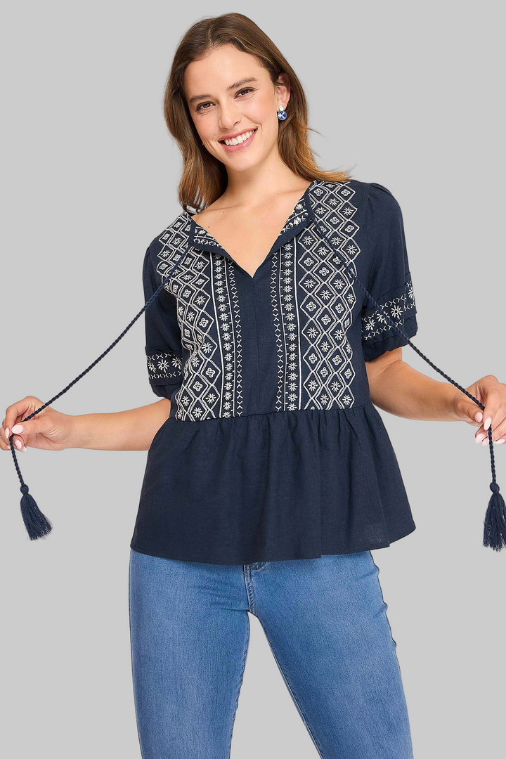 Woman wearing a navy blue blouse with white embroidery and holding tassels, on a white background.