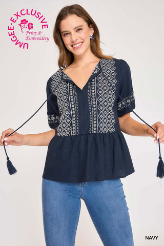 Woman wearing a navy blue blouse with white embroidery and holding tassels, on a white background.