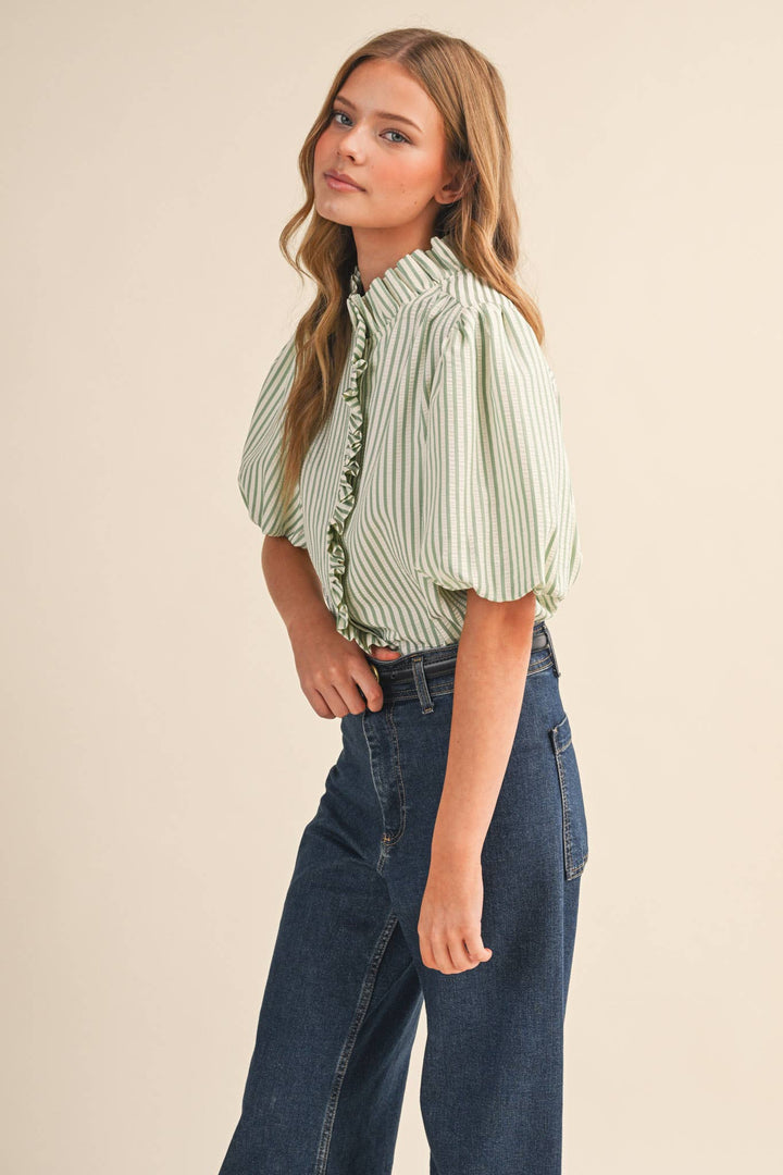 Woman wearing a green and white striped blouse with ruffled details and blue jeans on a beige background