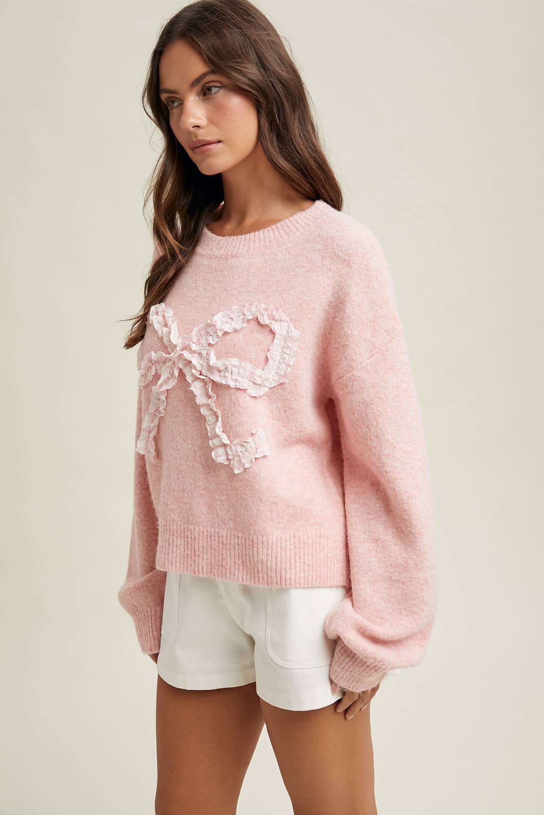 Woman wearing a pink sweater with floral embellishments on a beige background