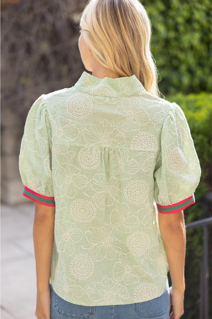 Woman wearing a light green floral blouse with red and green trim in an outdoor setting