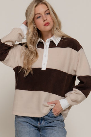 Woman wearing a brown and beige striped sweater with a white shirt underneath, standing against a plain background.