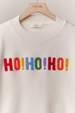 White sweater with colorful 'HO! HO! HO!' text on a hanger with 'mello' brand label.
