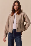 Woman wearing a beige jacket over a white shirt and blue jeans on a beige background