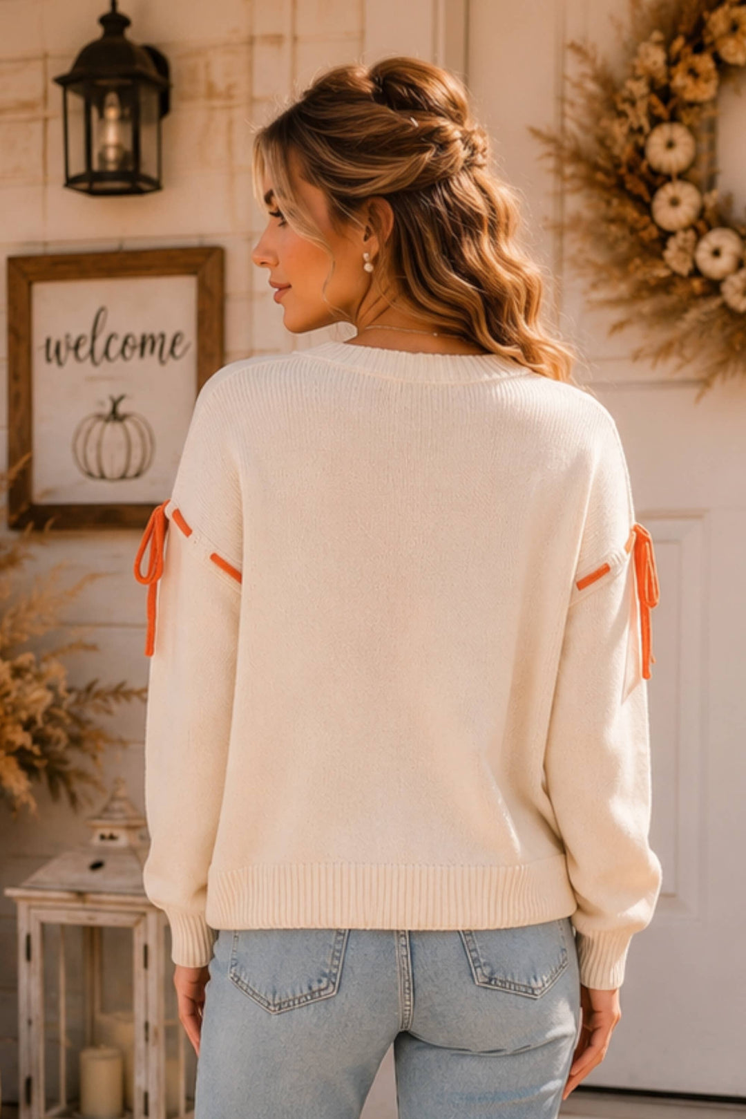 Woman wearing a cream sweater with orange accents in a home setting.
