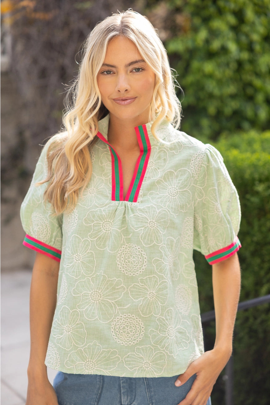 Woman wearing a light green blouse with red and green trim outdoors