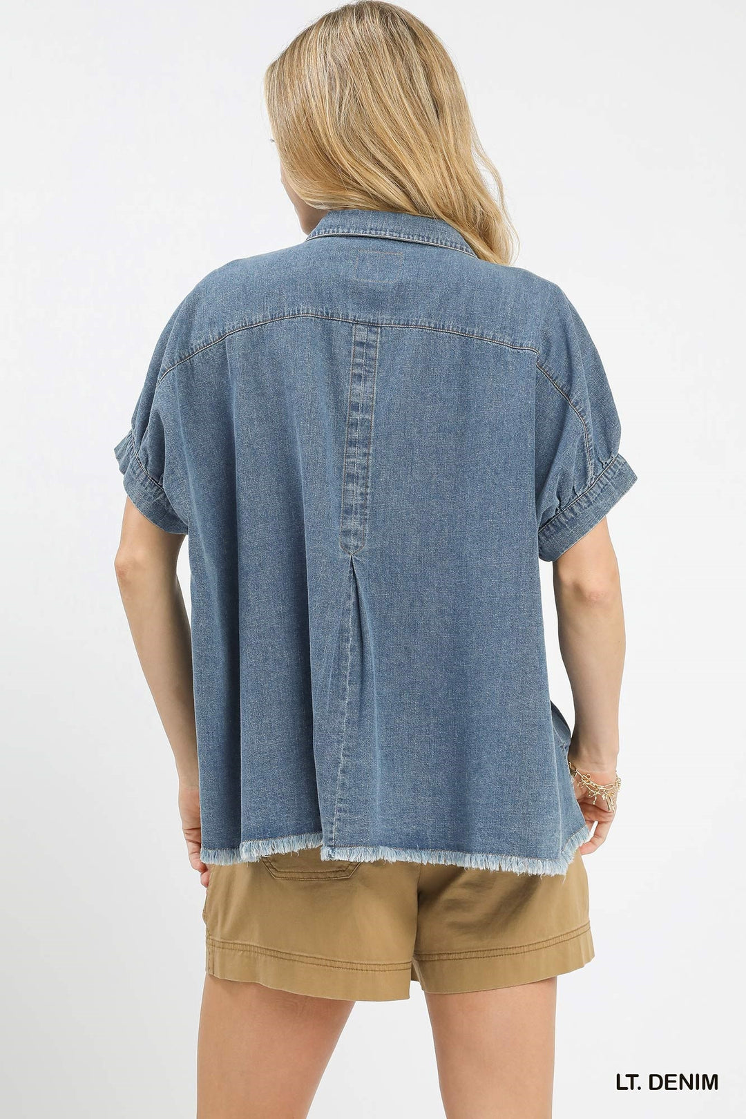 Person wearing a light denim shirt and beige shorts on a white background