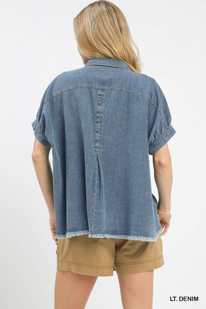 Person wearing a light denim shirt and beige shorts on a white background