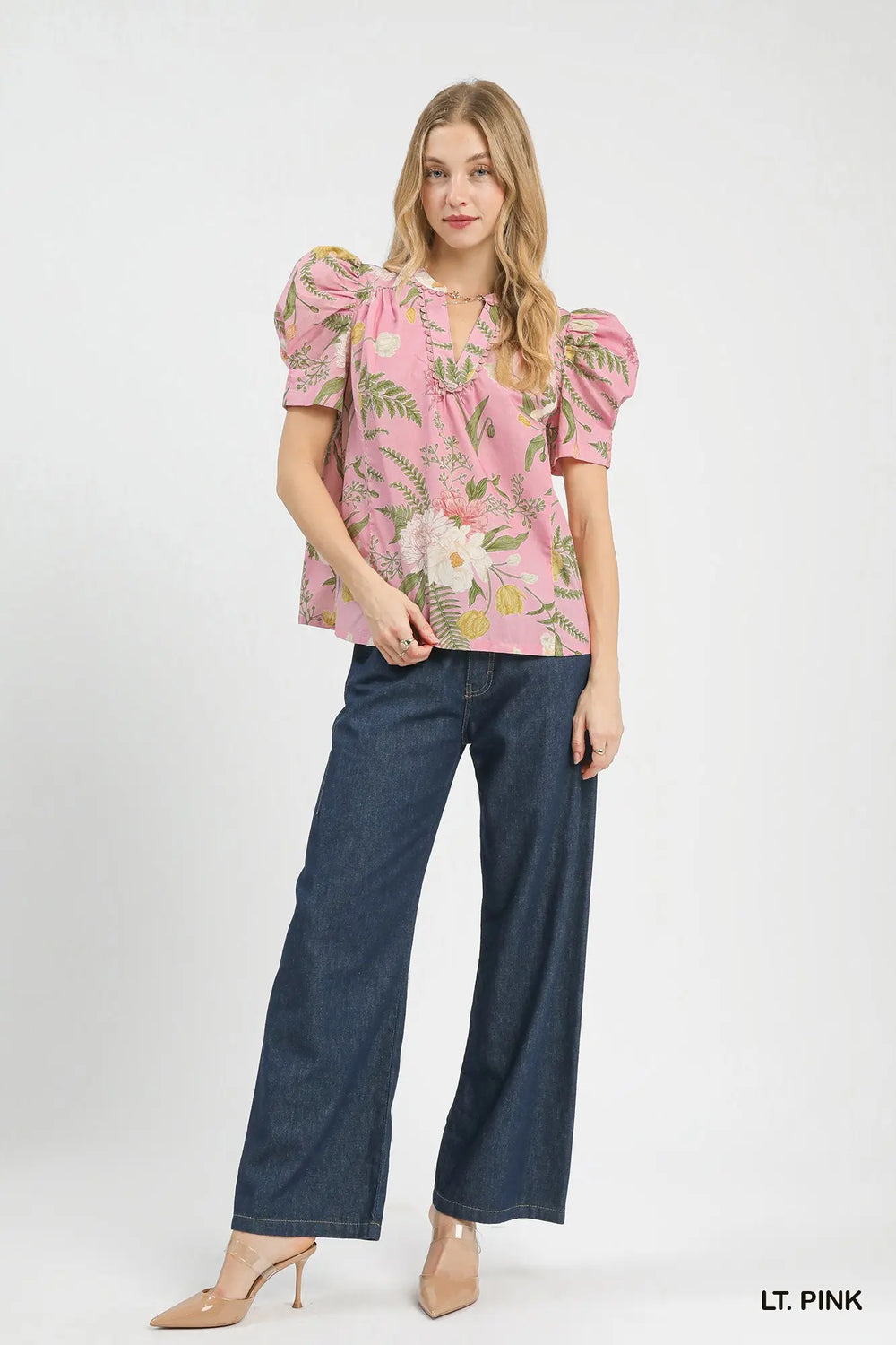 Woman wearing a light pink floral blouse and dark blue jeans on a white background