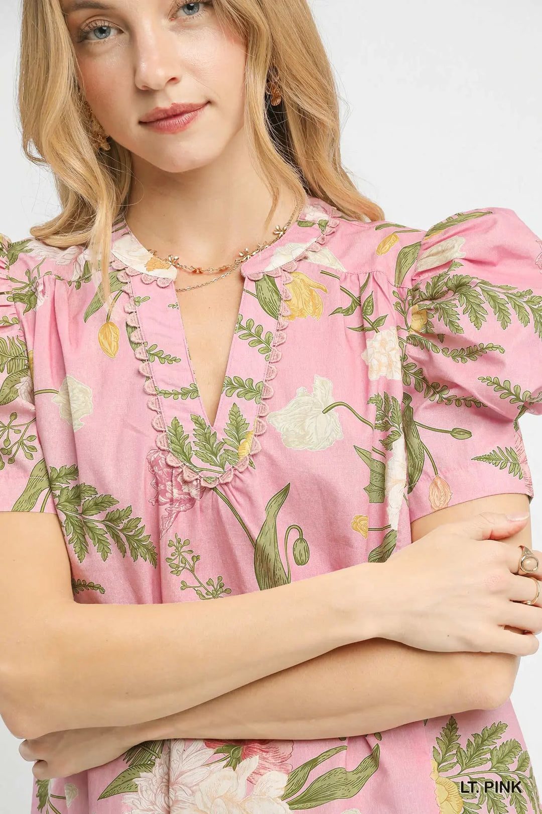 Woman wearing a pink floral dress with green leaves and white flowers.