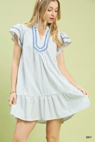 Woman wearing a white dress with blue stripes and ruffled details on a light green background