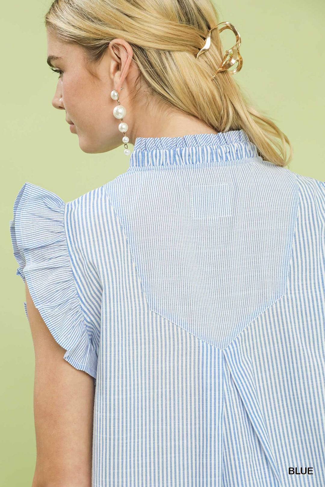 Woman wearing a blue and white striped shirt with ruffled sleeves on a light green background