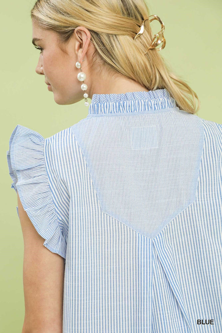 Woman wearing a blue and white striped shirt with ruffled sleeves on a light green background