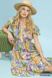 Woman wearing a floral dress and straw hat sitting on a green cushion against a light blue background