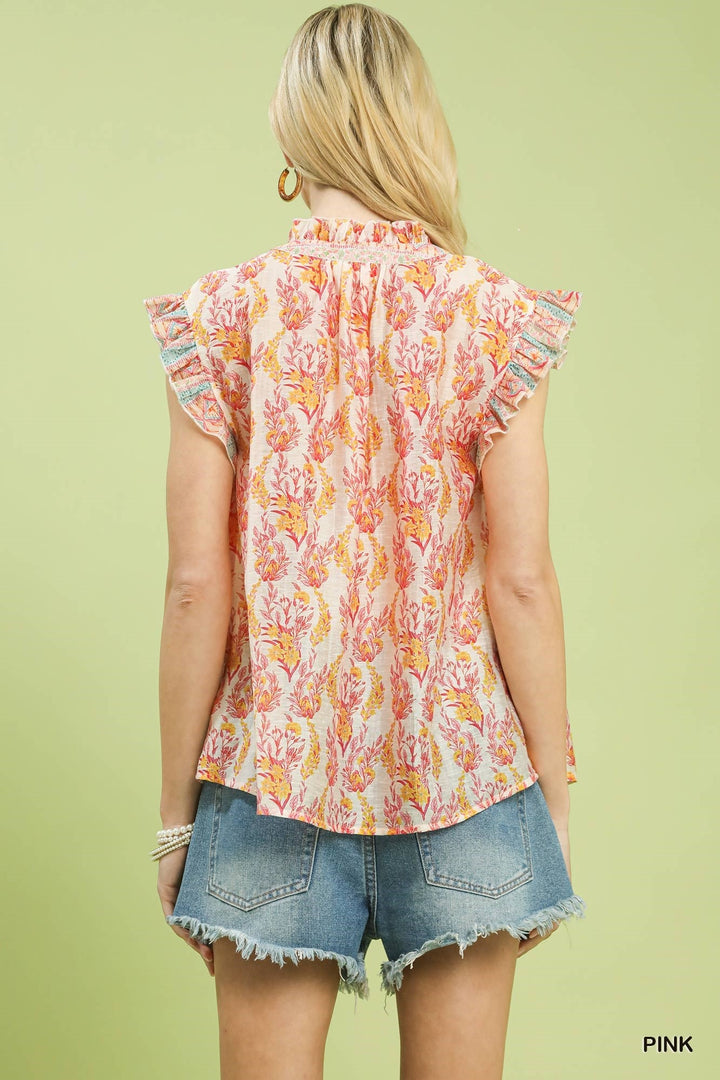 Woman wearing a sleeveless floral top and denim shorts on a light green background