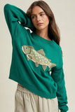 Woman wearing a green sweater with a fish design on a beige background