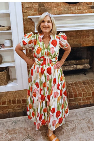 Woman wearing a floral dress standing in a room with a fireplace.