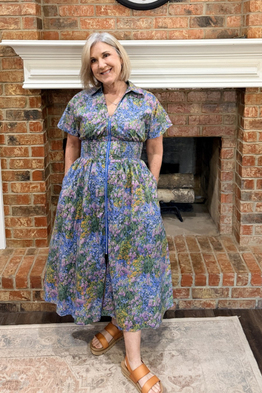 Woman wearing a floral dress standing in front of a brick fireplace.