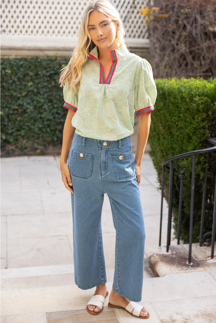 Woman wearing a light green blouse with red and navy trim and blue jeans, standing outdoors.