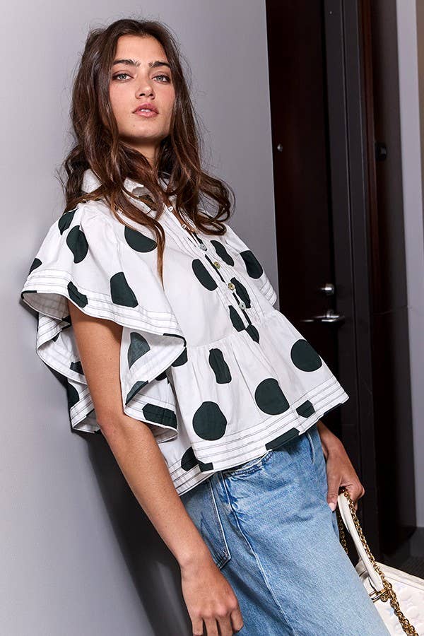 Woman wearing a white blouse with black polka dots and blue jeans against a neutral background