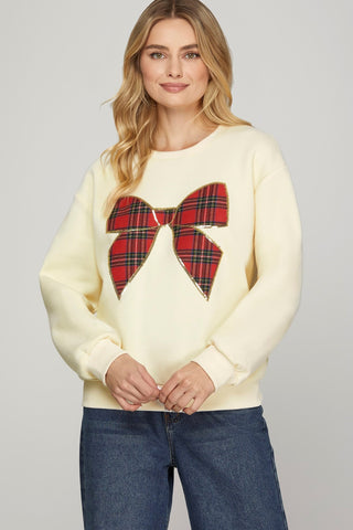 Woman wearing a cream sweater with a red tartan bow design on a plain background