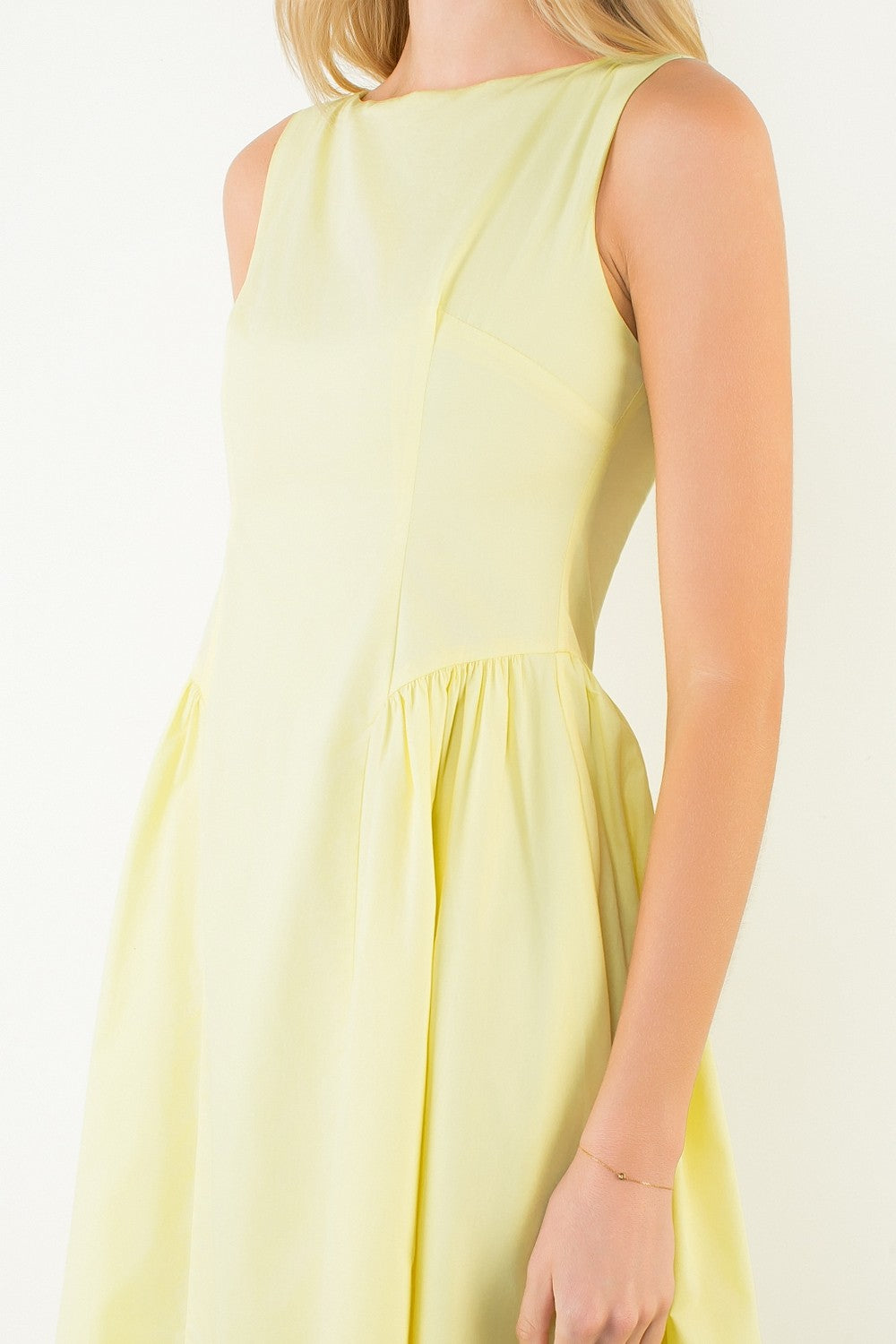 Woman in a light yellow dress standing outdoors with plants around
