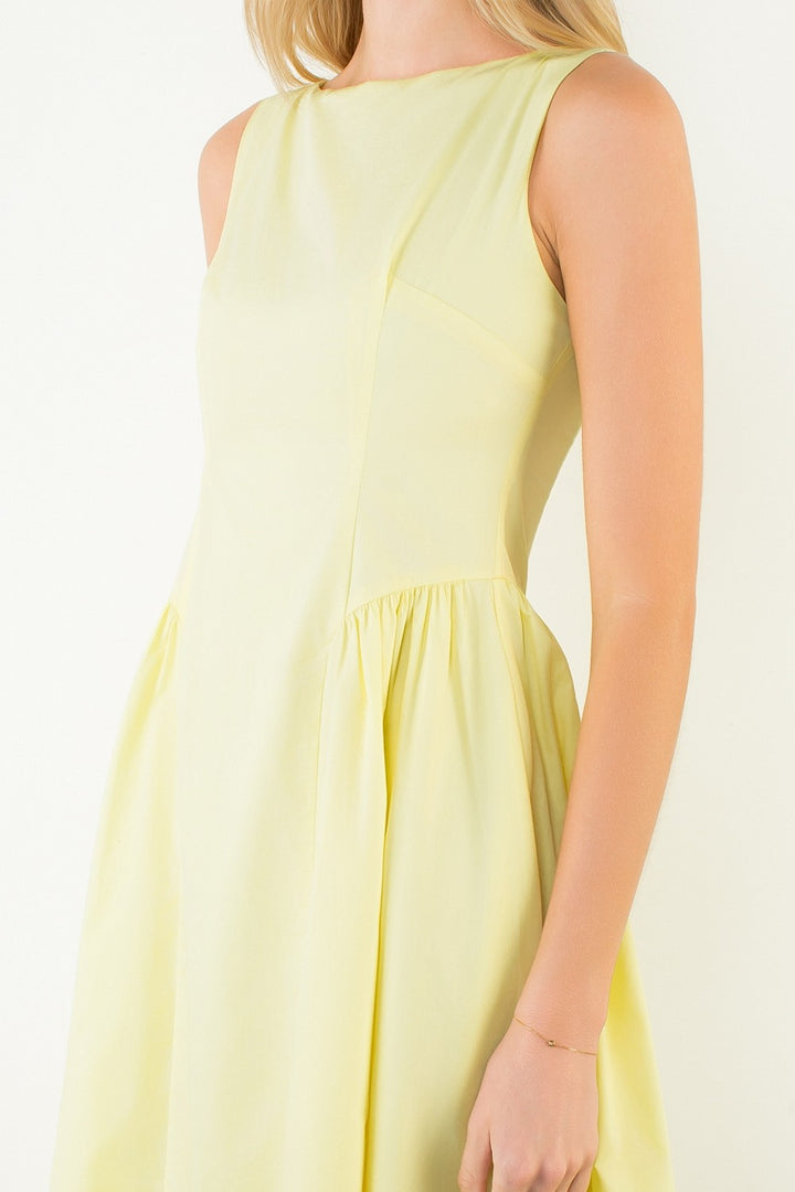 Woman in a light yellow dress standing outdoors with plants around