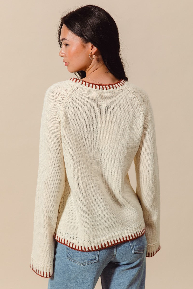 Woman wearing a cream sweater with red trim on a beige background