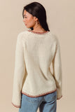 Woman wearing a cream sweater with red trim on a beige background