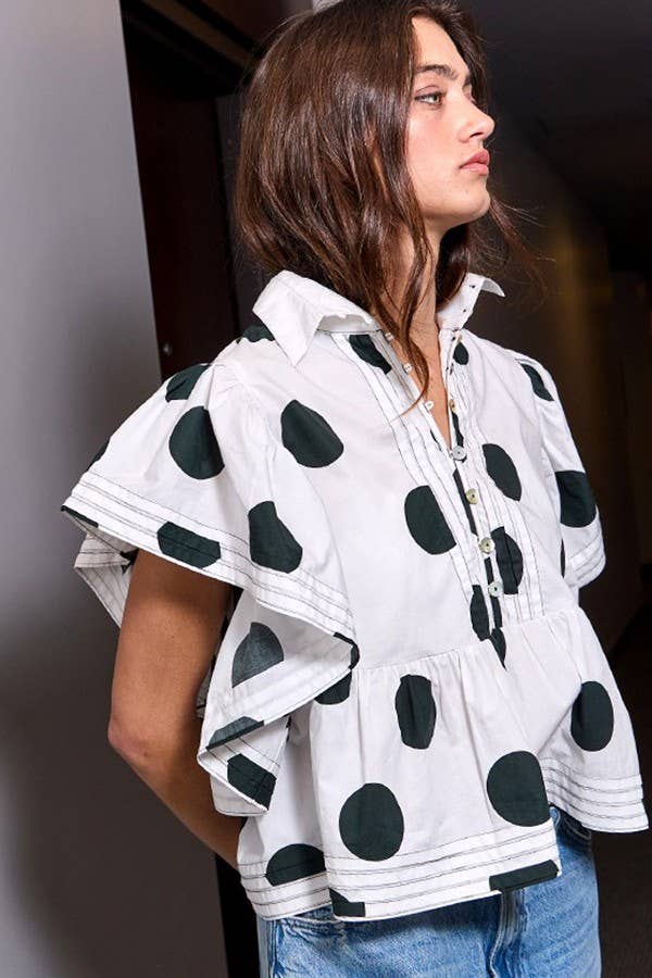 Woman wearing a white jacket with black polka dots and blue jeans.
