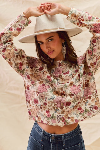 Woman wearing a floral sweater and wide-brimmed hat against a neutral background