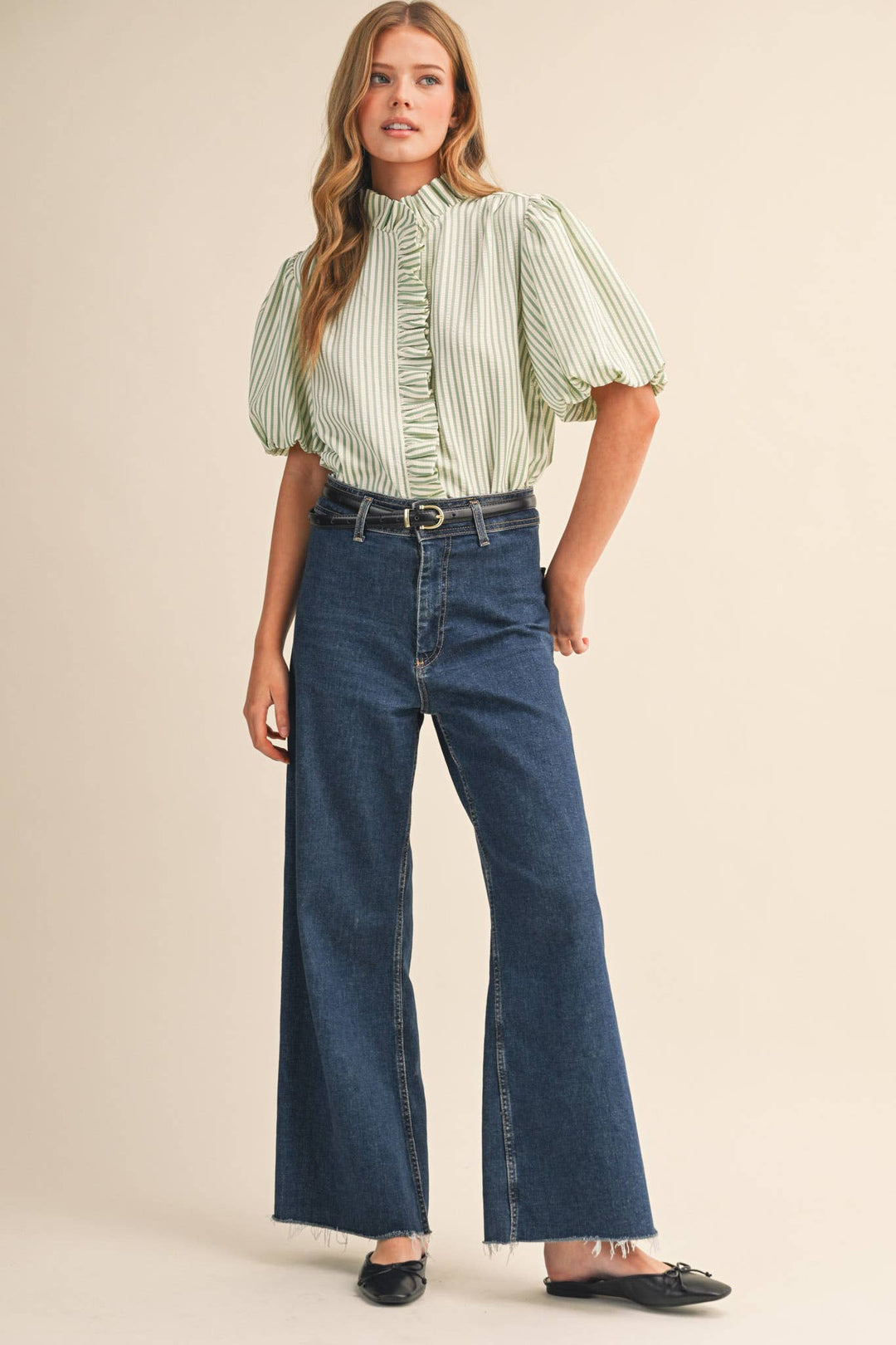 Woman wearing a green and white striped blouse and blue jeans on a beige background