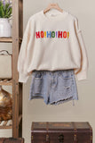 Beige sweater with 'HO! HO! HO!' text and denim shorts on a hanger against a neutral background.