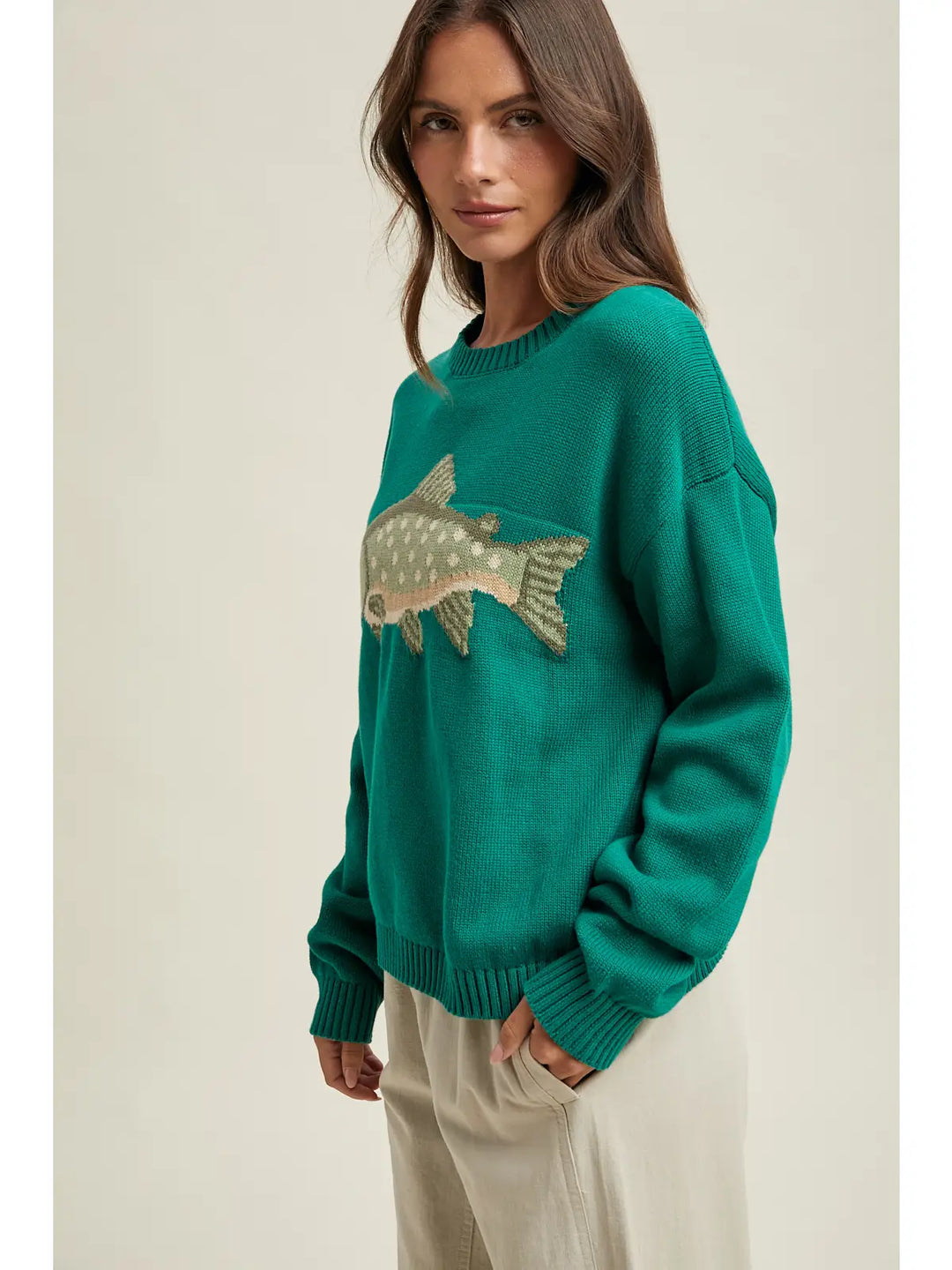Woman wearing a teal sweater with a fish design on a beige background