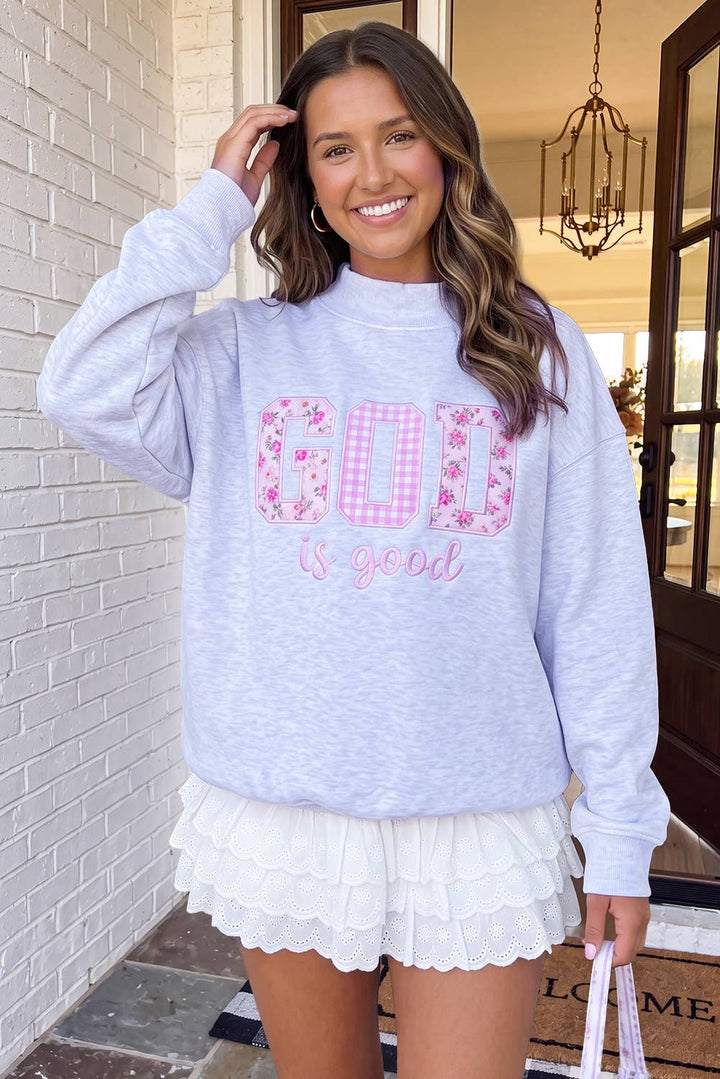 A woman wearing a light heather gray sweatshirt with a pink floral and gingham &