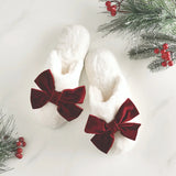 White slippers with red velvet bows on a white background with Christmas decorations.