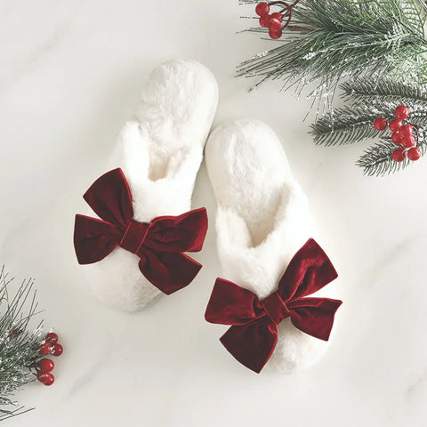 White slippers with red velvet bows on a white background with Christmas decorations.