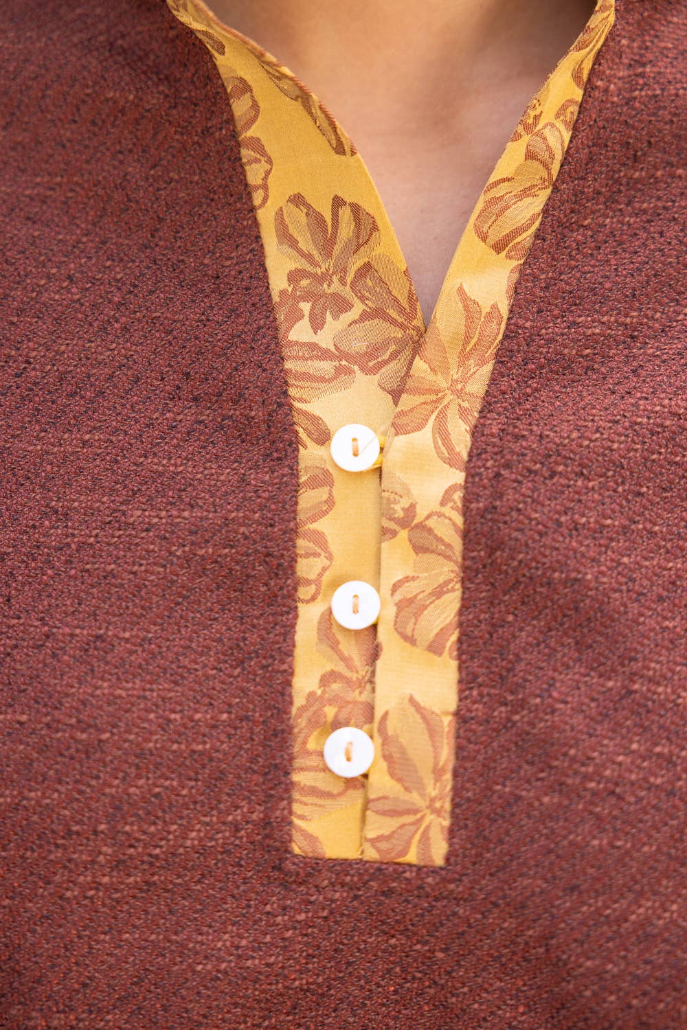 Close-up of a textured rust-brown knit top with a contrasting yellow floral V-neck trim and four white buttons.