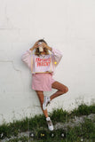 Person wearing a 'Parent' t-shirt and pink shorts lying on grass with a white wall background.