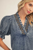 Woman wearing a blue denim blouse with embroidered details on a plain background