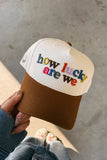 Cap with 'how lucky are we' text held by a person on a concrete surface
