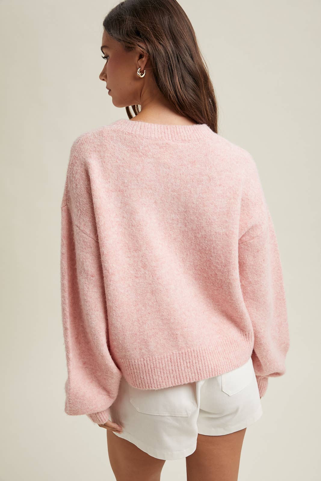 Woman wearing a pink sweater and white shorts on a plain background