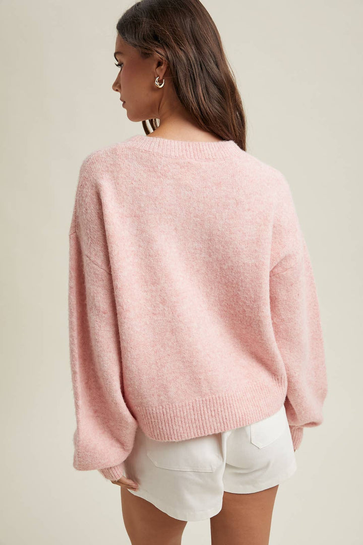 Woman wearing a pink sweater and white shorts on a plain background