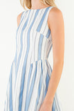Woman wearing a sleeveless dress with blue and white vertical stripes on a plain background